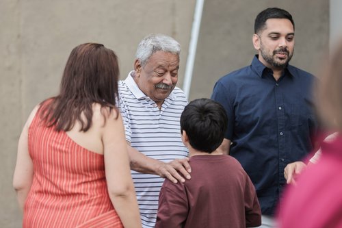 An older man smiles and places a hand on a boy's shoulder during a family gathering.